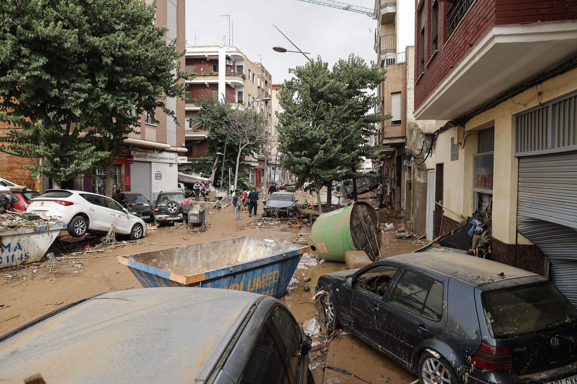 Unas personas caminan por una calle cubierta de lodo y llena de coches amontonados tras las intensas lluvias por la fuerte dana que afecta especialmente el sur y el este de la península ibérica, este miércoles en Valencia. EFE.